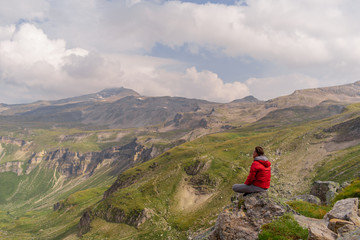 Obraz premium Young man in a red jacket on the stones looks at a magnificent view of the Alps mountains.