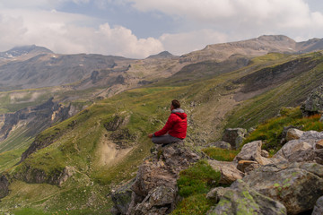 Fototapeta premium Young man in a red jacket on the stones looks at a magnificent view of the Alps mountains.