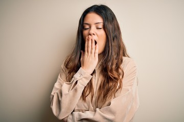 Young beautiful brunette woman wearing casual shirt standing over white background bored yawning tired covering mouth with hand. Restless and sleepiness.