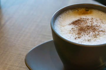 Delicious cappuccino with cinnamon and milk foam in dark cup on wooden table