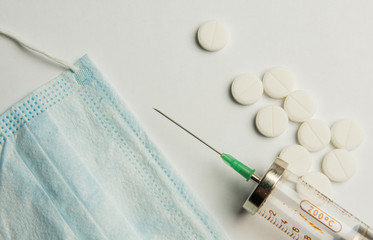 A syringe, a medical mask, and pills are on the table. Coronavirus