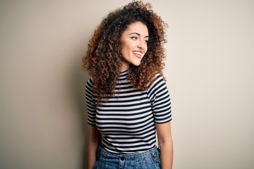 Young beautiful woman with curly hair and piercing wearing casual striped t-shirt looking away to side with smile on face, natural expression. Laughing confident.