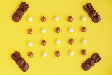 Easter eggs and bunny shaped sweets of milk chocolate laying in rows on yellow background.Religious holiday greeting card.Rabbit composition for congratulations.Symbol of celebration Sunday of Christ