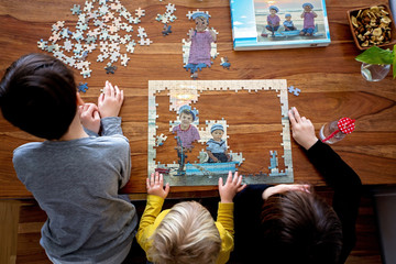 Three children, boys, assembling puzzle with their picture from the beach, playing at home