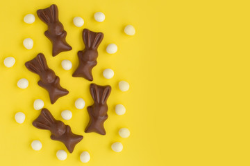 Easter white eggs and bunny shaped sweets of milk chocolate on yellow background. Religious holiday greeting card. Rabbit composition for congratulations. Symbol of celebration Sunday of Christ