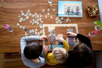 Three children, boys, assembling puzzle with their picture from the beach, playing at home