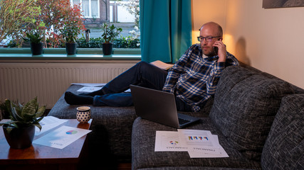 Fototapeta premium Man with beard calling with smartphone at home from the couch. Businessman working at home with paperworks and documents on the couch.