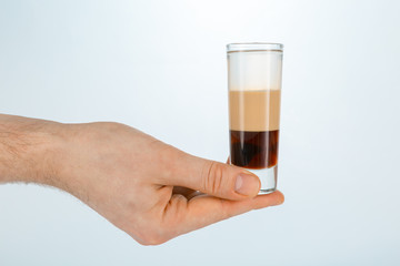 Close up of a hand holding a glass of b-52 cocktail on white background with copy space.