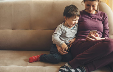 Caucasian mother and her small boy using a mobile on the sofa and smiling cheerfully