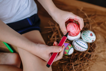 Hands of a child sitting on the kitchen table, paint a marker Easter egg.