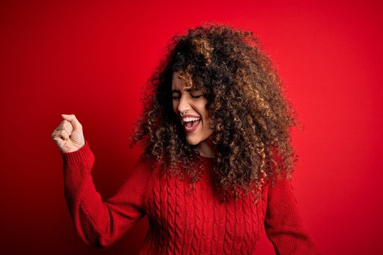 Young beautiful woman with curly hair and piercing wearing casual red sweater Dancing happy and cheerful, smiling moving casual and confident listening to music - Powered by Adobe