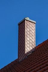 Tiled roof with a new chimney against a blue sky