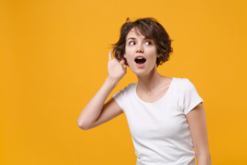 Curious young brunette woman girl in white t-shirt posing isolated on yellow orange wall background...