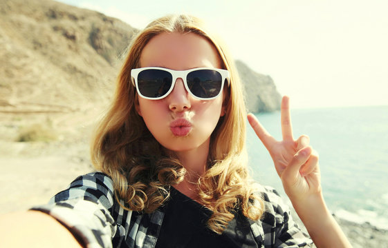 Portrait of happy woman blowing lips sending sweet air kiss stretching hand for taking selfie over sea background