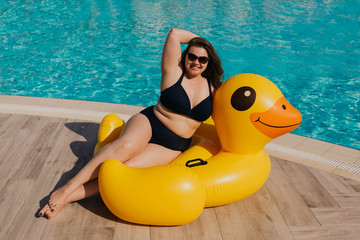 Curvy woman resting by the pool with yellow inflatable duck.