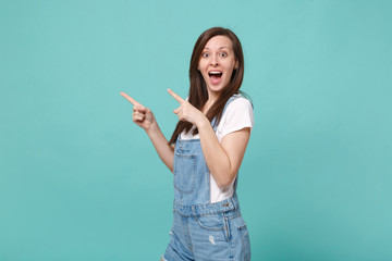 Surprised young brunette woman girl in casual denim clothes posing isolated on blue turquoise wall background in studio. People lifestyle concept. Mock up copy space. Pointing index fingers aside up.