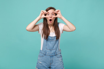 Shocked young brunette woman girl in casual denim clothes posing isolated on blue turquoise background in studio. People lifestyle concept. Mock up copy space. Stretching eyelids, keeping mouth open.