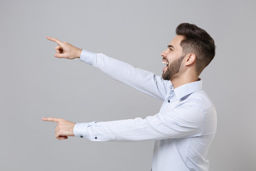 Side view of funny young unshaven business man in light shirt posing isolated on grey background in studio. Achievement career wealth business concept. Mock up copy space. Point index fingers aside.