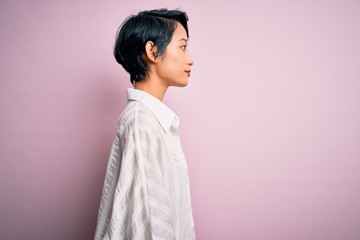 Young beautiful asian girl wearing casual shirt standing over isolated pink background looking to...