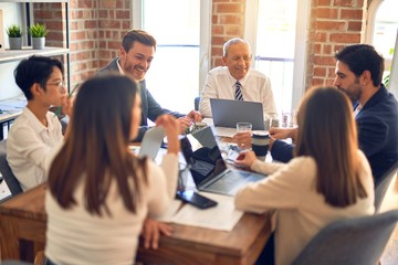 Group of business workers working together. Sitting on desk using laptop and talking at the office