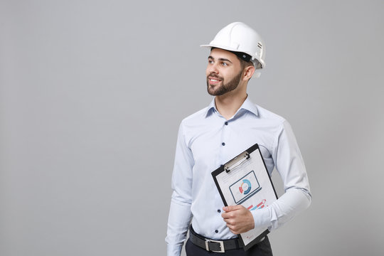 Handsome Business Man In Light Shirt, Protective Construction White Helmet Isolated On Grey Background. Achievement Career Wealth Business Concept. Hold Clipboard With Papers Document Looking Aside.