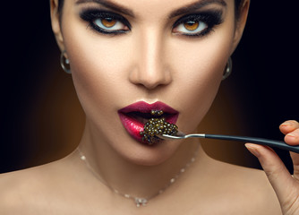Beautiful Fashion Model woman eating black caviar. Beauty girl portrait with caviar on her lips....