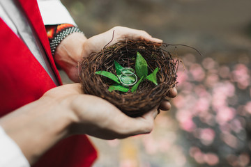 Wicker handmade nest with wedding rings in priest hands. Traditional spiritual wedding ceremony in religious rites. Symbol of love and commitment.