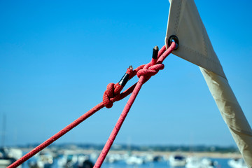 View of boat sail furled with red sail sheets with blue sky and out of focus boats in the background