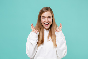 Fototapeta premium Cheerful young woman girl in casual white hoodie isolated on blue turquoise background. People lifestyle concept. Mock up copy space. Waiting for special moment keeping fingers crossed making wish.