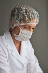 Doctor with face covered with mask. Portrait of young woman wearing the uniform and mask to avoid virus infection and to prevent the spread of disease. Real people, authentic situations