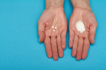 Female hands with sugar and pills on blue background. Choice of sweetener in tablets or regular sugar.