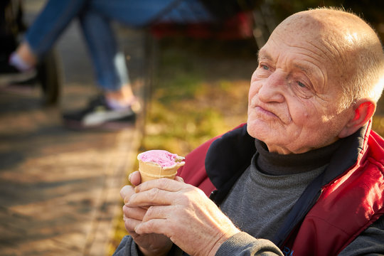 Eighty-year-old man walks in a public park, eats ice cream in a waffle cup