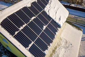 Close up surface of a house roof covered with solar panels in winter with snow on top. Energy...