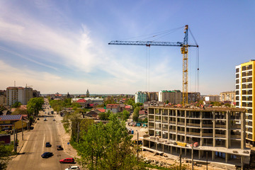 Apartment or office tall building under construction. Working builders and tower cranes on bright...
