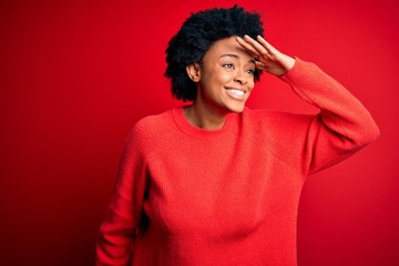 Fototapeta na wymiar Young beautiful African American afro woman with curly hair wearing casual sweater very happy and smiling looking far away with hand over head. Searching concept.
