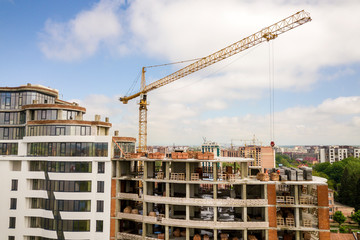 Apartment or office tall building under construction. Brick walls, glass windows, scaffolding and concrete support pillars. Tower crane on bright blue sky copy space background.