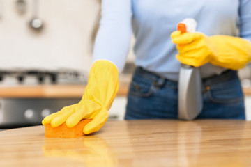 Young woman cleaning kitchen table using spray and sponge