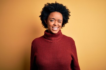 Fototapeta na wymiar Young beautiful African American afro woman with curly hair wearing casual turtleneck sweater winking looking at the camera with sexy expression, cheerful and happy face.