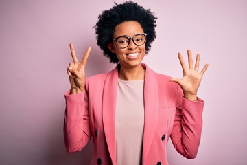 Young beautiful African American afro businesswoman with curly hair wearing pink jacket showing and pointing up with fingers number seven while smiling confident and happy.