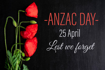 Anzac day. Greeting card with the inscription and poppy flowers on a black background. Flat lay,...