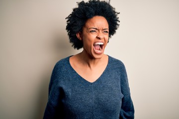 Fototapeta na wymiar Young beautiful African American afro woman with curly hair wearing casual sweater angry and mad screaming frustrated and furious, shouting with anger. Rage and aggressive concept.