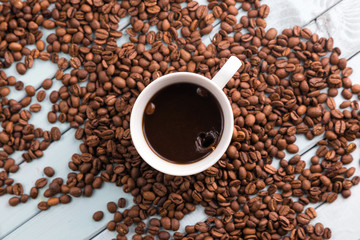 Coffee beans are spilled on the wooden table. White coffee Cup. Top view of the still life. Turquoise boards.