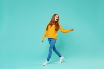 Fototapeta na wymiar Cheerful young redhead woman girl in yellow sweater posing isolated on blue turquoise background studio portrait. People emotions lifestyle concept. Mock up copy space. Pointing index finger aside.