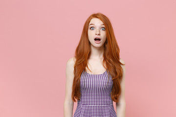 Shocked young redhead woman girl in plaid dress posing isolated on pastel pink wall background studio portrait. People sincere emotions lifestyle concept. Mock up copy space. Keeping mouth open.