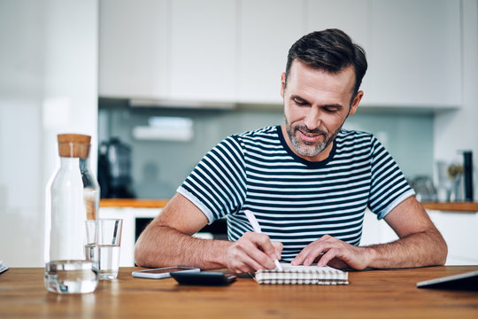 Picture of happy man managing personal budget with calculator and notebook