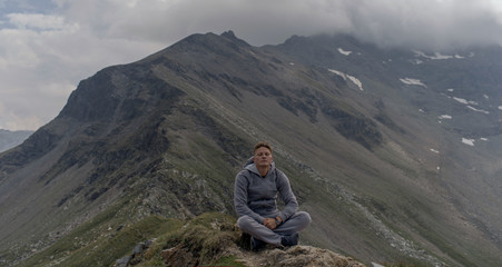 Naklejka na ściany i meble Young man meditates on the top of Alpine mountains.