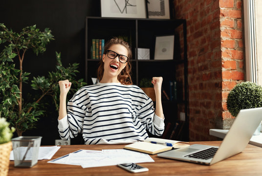 Excited woman celebrating victory while working at laptop in loft office