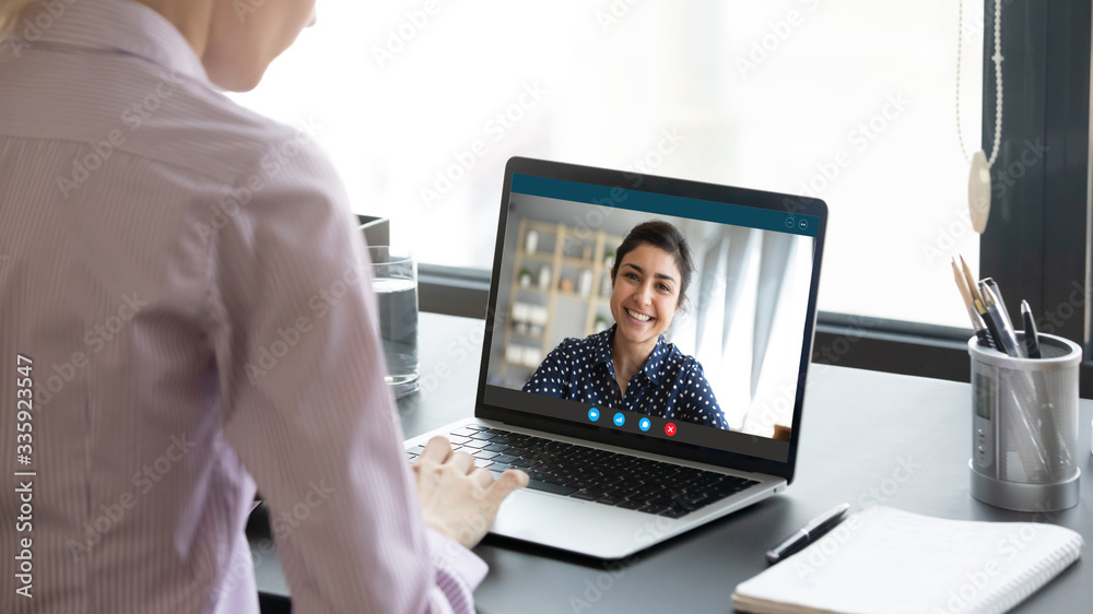 Wall mural indian girl communicate with friend on-line by video call, pc screen view over female shoulder. ment