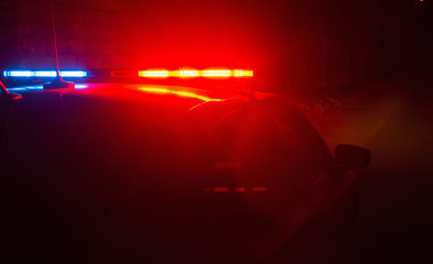 Police car with red and blue flashing lights on empty night street background, crime scene, night patrolling the city, fight against looting during quarantine. © Evgen