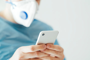 Close up detail of male doctor with mask and biohazard suit using the smartphone over white...